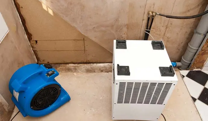 Air mover and dehumidifier drying the area under a basement stairway in a Papillion home after a water loss