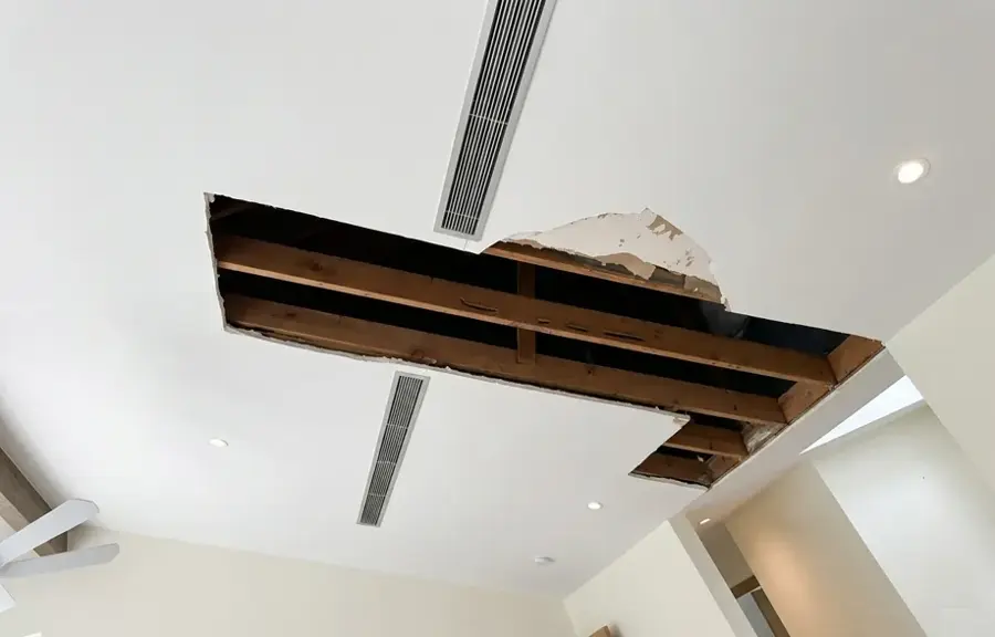 Ceiling drywall cut open to expose wet joists after a leak from above