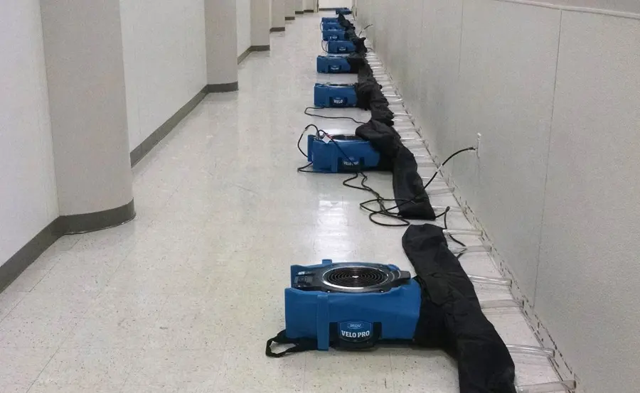 Row of air movers drying the base of the walls along a long commercial corridor